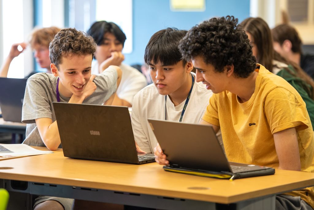 Three sixth formers confer around a laptop.